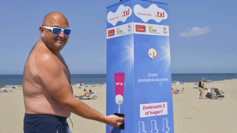 Man smeert zich in bij een Smeerkees zonnebrandpaal van GGD Hollands Noorde op het strand.